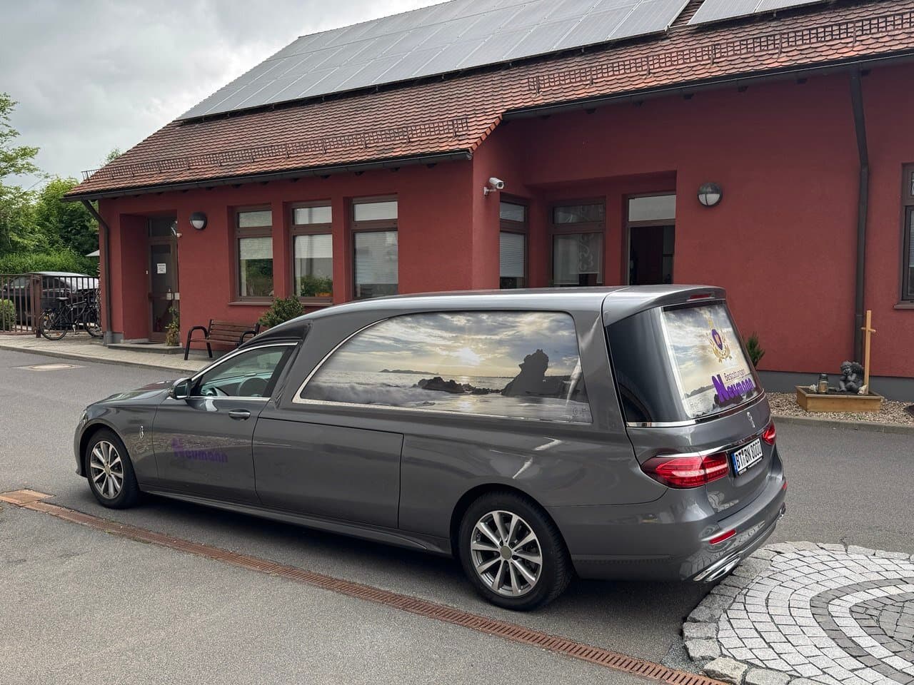 Bestattungswagen parkt vor Gebäude mit Solaranlage
