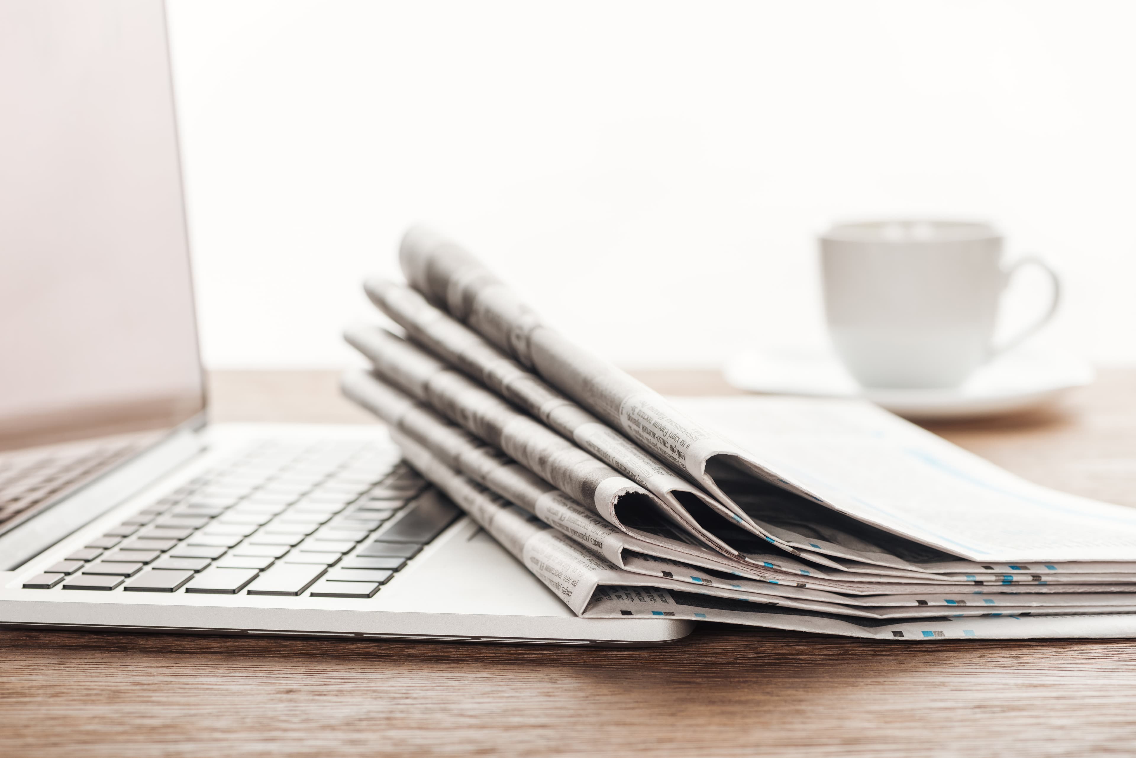 Laptop mit Zeitungsstapel und Kaffeetasse